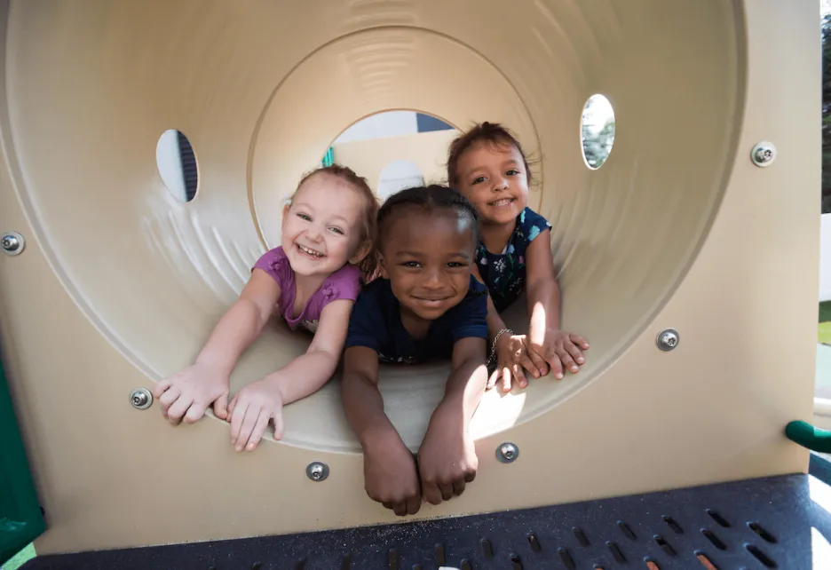 Three kids in Pre-K playing in a tunnel on a playground.