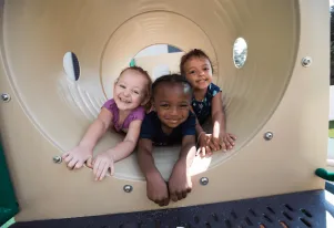 Three kids in Pre-K playing in a tunnel on a playground.