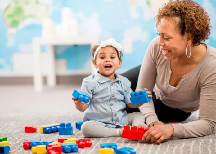 baby playing with blocks as a woman looks on.